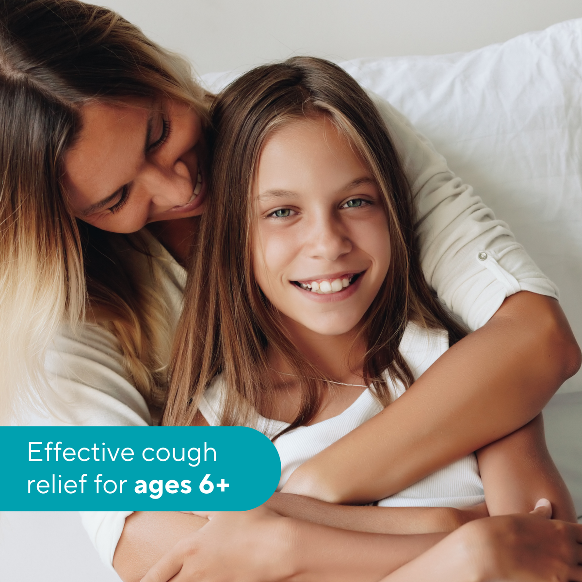 A smiling young girl in a white shirt hugs a woman in a white top on a white bed, with a teal text banner that reads 'Effective cough relief for ages 6+'.