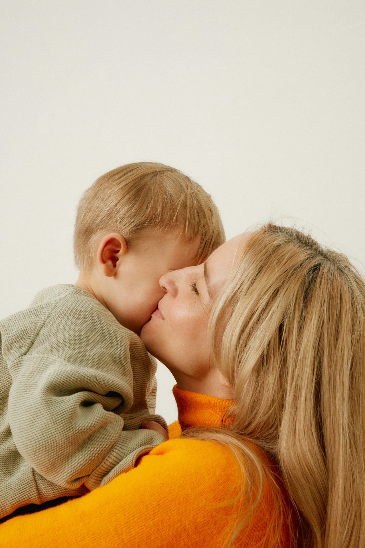 Woman kissing a child on the forehead against a plain background