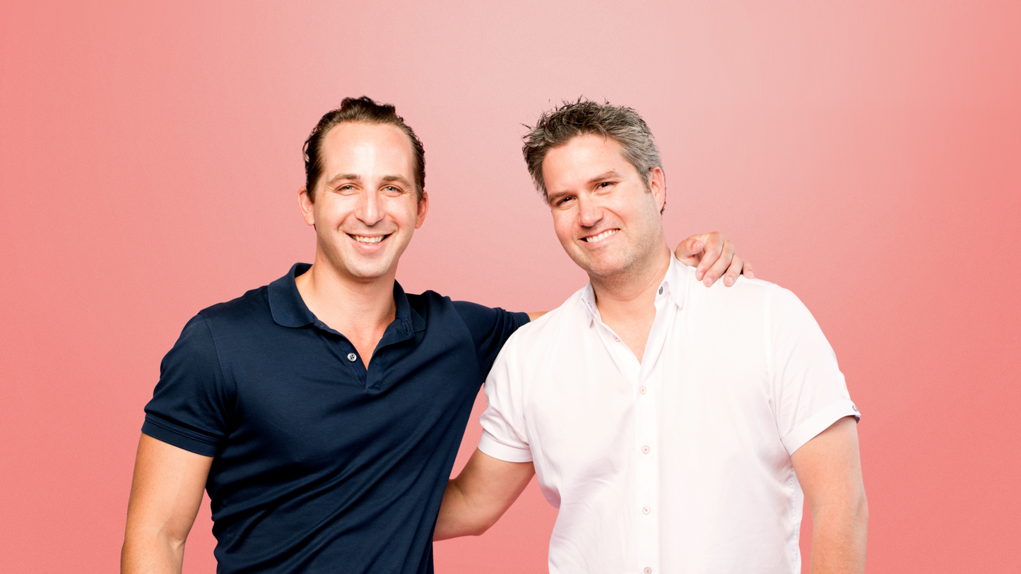 Two men standing close together against a pink background
