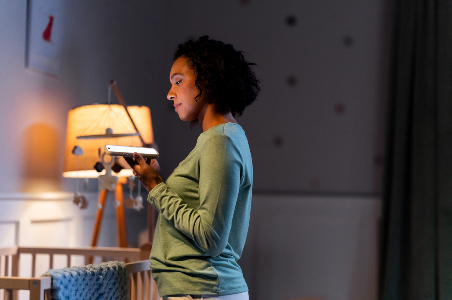 Woman using a smartphone in a room with a lamp and chair.